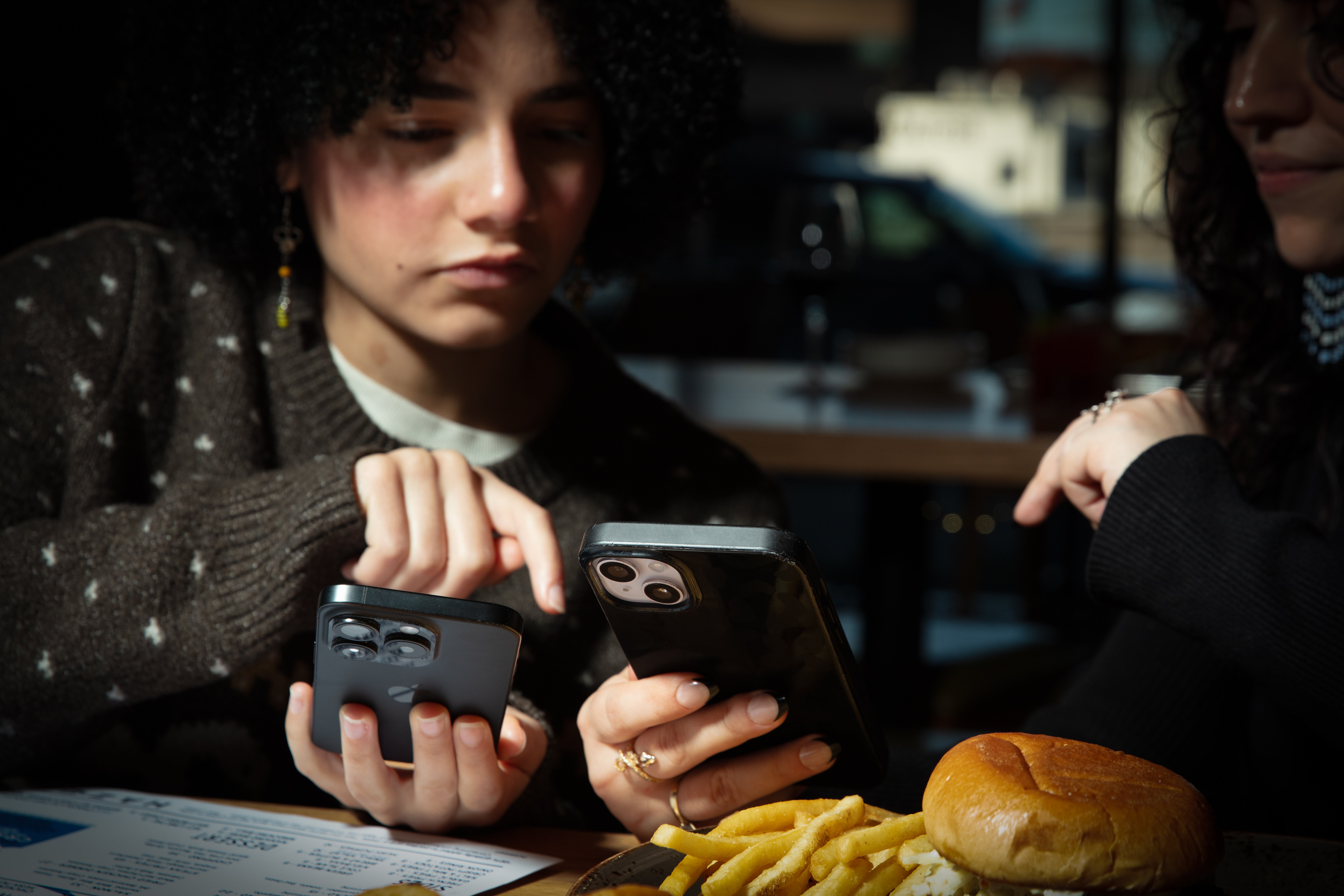 Two teens at table with food and phones